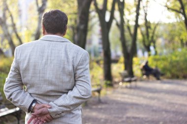 Kıdemli adam yürüyor, elleri bağlı. Kıdemli adam parkta yürüyor ve dinleniyor.