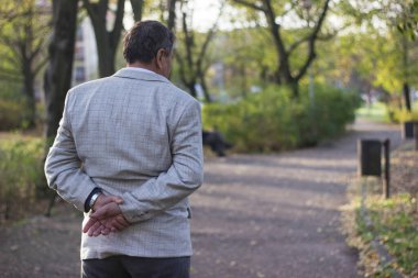 Kıdemli adam yürüyor, elleri bağlı. Kıdemli adam parkta yürüyor ve dinleniyor.