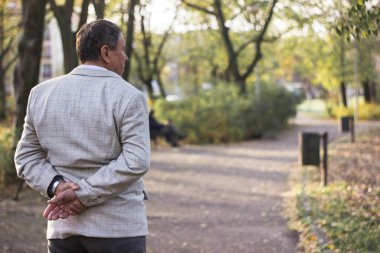 Kıdemli adam yürüyor, elleri bağlı. Kıdemli adam parkta yürüyor ve dinleniyor.