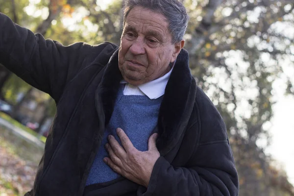 Senior man suffering from heart attack, outdoors. Elderly man having chest pains or heart attack in the park. Man clutching his chest. Pain, possible heart attack