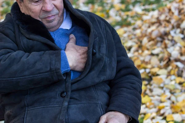 Senior man suffering from heart attack, outdoors. Elderly man having chest pains or heart attack in the park. Man clutching his chest. Pain, possible heart attack