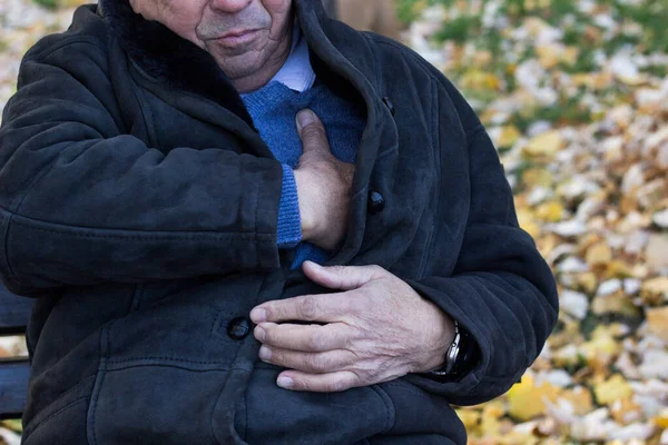 Senior man suffering from heart attack, outdoors. Elderly man having chest pains or heart attack in the park. Man clutching his chest. Pain, possible heart attack