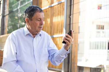 Kıdemli adam ve akıllı telefonu. Modern olgun bir adam açık havada akıllı telefon kullanırken eğlenir.