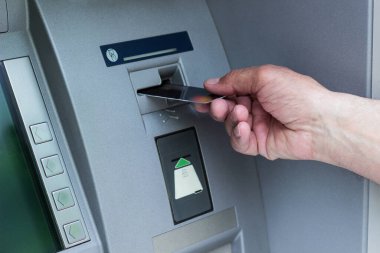 ATM kullanan kıdemli bir adamın eli. Son sınıf öğrencisi ATM 'ye kredi kartı koyuyor.
