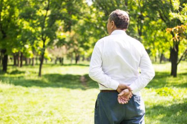 Kıdemli adam yürüyor, elleri bağlı. Kıdemli adam parkta yürüyor ve dinleniyor.