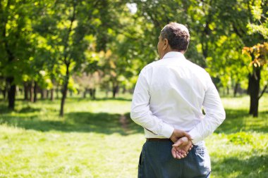 Kıdemli adam yürüyor, elleri bağlı. Kıdemli adam parkta yürüyor ve dinleniyor.