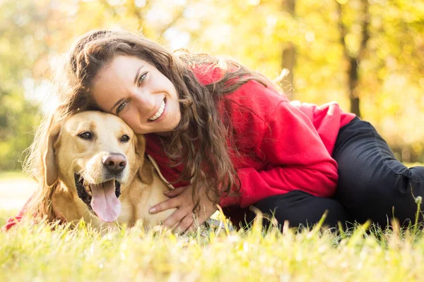 Parkta sevimli köpeğiyle gülümseyen genç bir kadın.