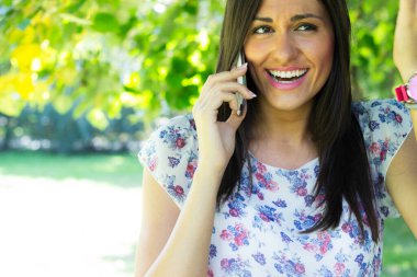 Dışarıda güneşin tadını çıkaran bir kadın, akıllı telefonunu kullanıyor.