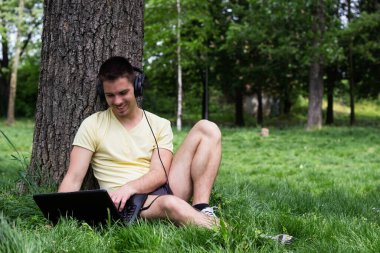Güzel, genç bir erkek parkta oturmuş dizüstü bilgisayarla sohbet ediyor.