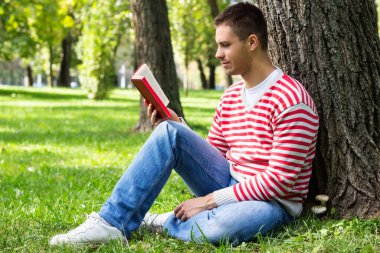 Gitmek için bir kitap ve kahve ile bir parkta oturan genç adam