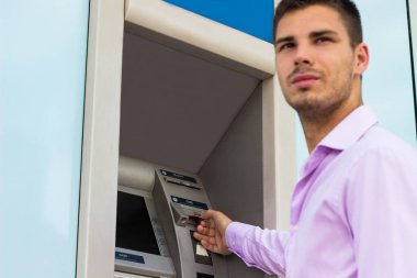Genç işadamı bir para çekme makinesinden para çekiyor.