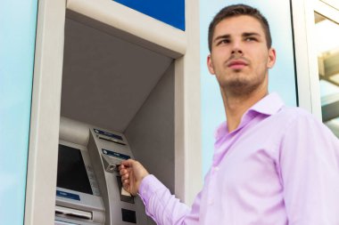 Genç işadamı bir para çekme makinesinden para çekiyor.