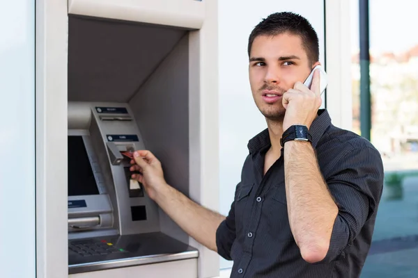 Młody Człowiek Rozmawia Przez Telefon Wkłada Kartę Kredytową Bankomatu — Zdjęcie stockowe