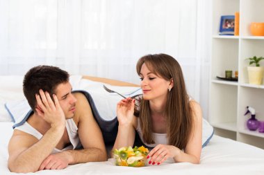 Yatak odasında meyve salatası yiyen genç bir çift.