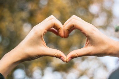 Elleriyle kalp sembolü. Doğa bokeh arkaplanı