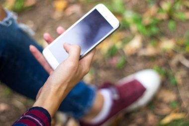 Parkta akıllı telefon kullanan genç bir kadın.