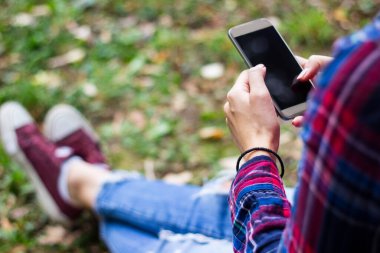 Parkta akıllı telefon kullanan genç bir kadın.