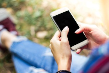 Parkta akıllı telefon kullanan genç bir kadın.