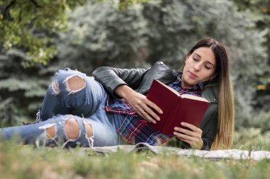 Woman reading a book while laying on the grass. Outdoors, in the park.