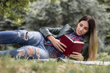 Woman reading a book while laying on the grass. Outdoors, in the park.