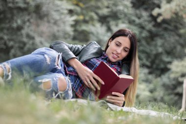 Woman reading a book while laying on the grass. Outdoors, in the park.