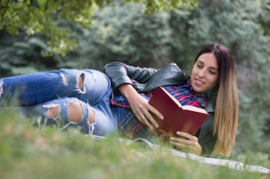 Woman reading a book while laying on the grass. Outdoors, in the park.