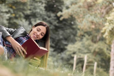 Woman reading a book while laying on the grass. Outdoors, in the park.