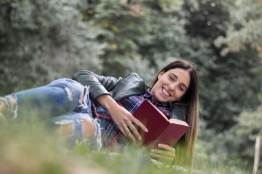Woman reading a book while laying on the grass. Outdoors, in the park.