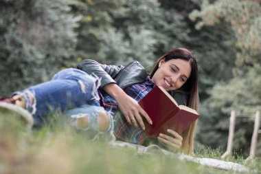 Woman reading a book while laying on the grass. Outdoors, in the park.