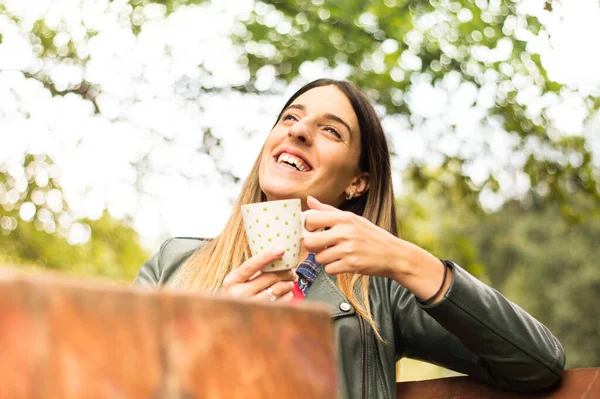 Pretty woman drinking coffee in the nature. Sitting, smiling and enjoying