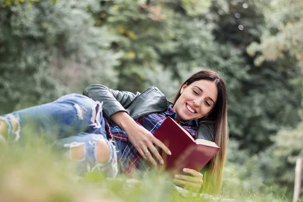 Woman reading a book while laying on the grass. Outdoors, in the park.