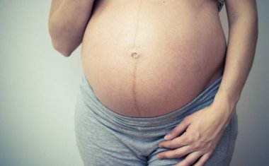 Hamile güzel bir kadın evde karnının üstünde el ele tutuşuyor. Duvarın yanında duran hamile kadın.