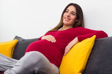 Pregnant beautiful woman holds hands on belly at home interiors. Resting at the home