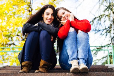 Two young smiling friends sitting on the stairs, autumn