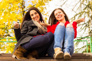 Two young smiling friends sitting on the stairs, autumn