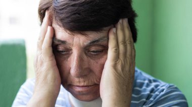 Baş ağrısı çeken ve evde şakaklarını ovuşturan bir kadının portresi.