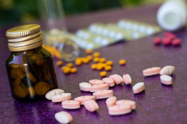 Tıbbi şişeler ve ilaç hapları mor arka plana dökülüyor.