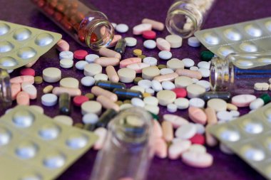 Tıbbi şişeler ve ilaç hapları mor arka plana dökülüyor.