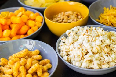 Koyu renkli masa üzerinde tuzlu abur cuburlar. Filmde patates cipsi, patlamış mısır, fıstık, peynir çubuğu, ketçap çubuğu, tzatziki cipsi, dumanlı fiske ve diğerleri yer alıyor.