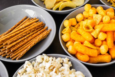 Koyu renkli masa üzerinde tuzlu abur cuburlar. Filmde patates cipsi, patlamış mısır, fıstık, peynir çubuğu, ketçap çubuğu, tzatziki cipsi, dumanlı fiske ve diğerleri yer alıyor.