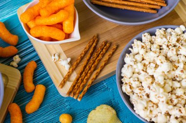 Ahşap masada bira tuzlu atıştırmalıklar. Koyu renkli masa üzerinde tuzlu abur cuburlar. Filmde patates cipsi, patlamış mısır, fıstık, peynir çubuğu, ketçap çubuğu, tzatziki cipsi, dumanlı fiske ve diğerleri yer alıyor.