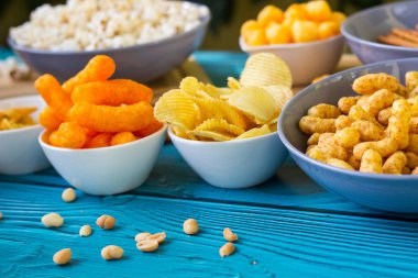 Ahşap masada bira tuzlu atıştırmalıklar. Koyu renkli masa üzerinde tuzlu abur cuburlar. Filmde patates cipsi, patlamış mısır, fıstık, peynir çubuğu, ketçap çubuğu, tzatziki cipsi, dumanlı fiske ve diğerleri yer alıyor.