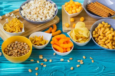 Ahşap masada bira tuzlu atıştırmalıklar. Koyu renkli masa üzerinde tuzlu abur cuburlar. Filmde patates cipsi, patlamış mısır, fıstık, peynir çubuğu, ketçap çubuğu, tzatziki cipsi, dumanlı fiske ve diğerleri yer alıyor.