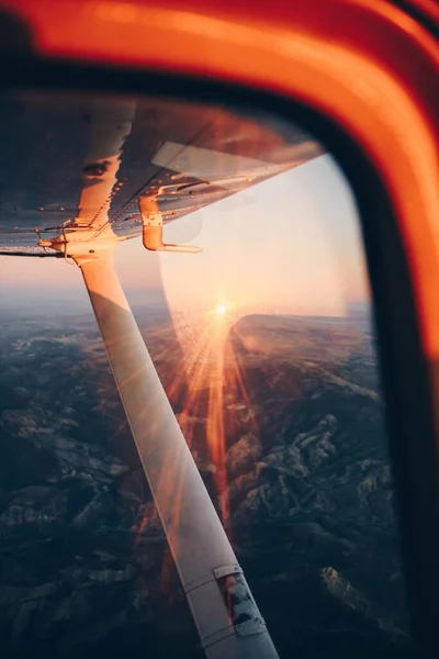 Vue de l'aile d'un petit avion volant au coucher du soleil sur la ville et le rivage de la mer — Photo