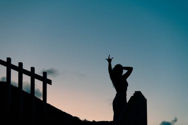 Gün batımının keyfini çıkaran kolları havada bir kızın arka ışıklandırılmış silueti
