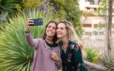 İki genç kız cep telefonuyla selfie çekiyor. Sosyal ağlarda arkadaşlık kavramı