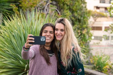 İki genç kız cep telefonuyla selfie çekiyor. Sosyal ağlarda arkadaşlık kavramı