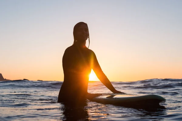 Chica surfista esperando una ola en el agua al atardecer —  Fotos de Stock