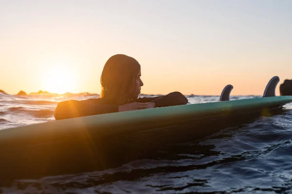 Chica surfista esperando una ola en el agua al atardecer —  Fotos de Stock