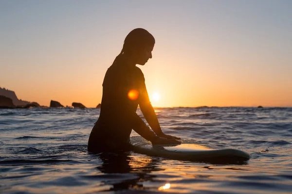 Szörfös lány várja a hullámot a vízben naplementekor — Stock Fotó